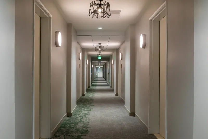 A long, quiet hotel hallway with carpeted floors and room doors on both sides